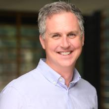 man smiling in a headshot wearing a blue button-down shirt.